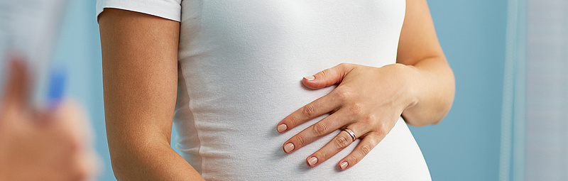 Schwangere Frau, die die Hände auf den Bauch gelegt hat und mit ihrem Frauenarzt spricht