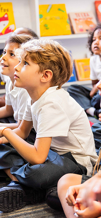 Eine Gruppe von Kindern sitzt am Boden und hören jemandem zu, der einen Vortrag hält