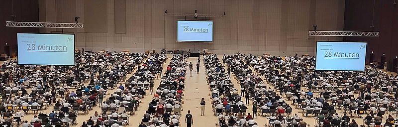 Teilnehmer*innen des MedAT 2025 sitzen in der Grazer Stadthalle an Tischen.