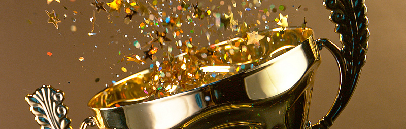 Ein Pokal aus dem Confetti sprüht auf goldenem Hintergrund